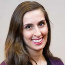 Woman with brown hair wearing a purple shirt smiling at camera