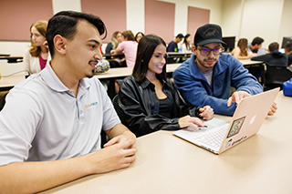 Three students in classroom looking at open laptop