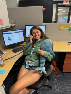 Student sitting on chair talking on phone and holding stuffed animal. 