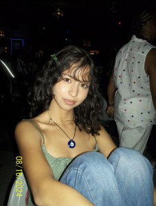 Student wearing green shirt and blue necklace looking directly at camera. 