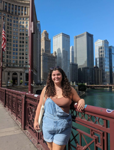 Student posing on bridge over water with large buildings in the background