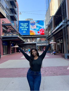 Student posing in city plaza holding up both arms. 