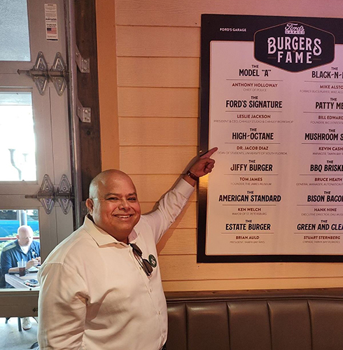 jacob diaz pointing to the burger named in is honor on the menu board hanging on the wall