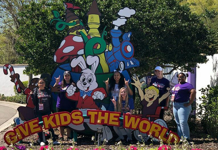 Students in front of a sign reading "Give Kids the World"