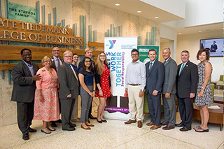Workgroup posing in front of a YMCA sign in the Kate Tiedemann College of Business